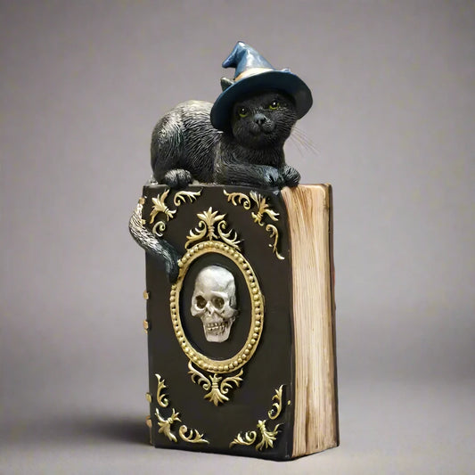 Decorative book with a skull design  with a cat perched on top wearing a witch hat 